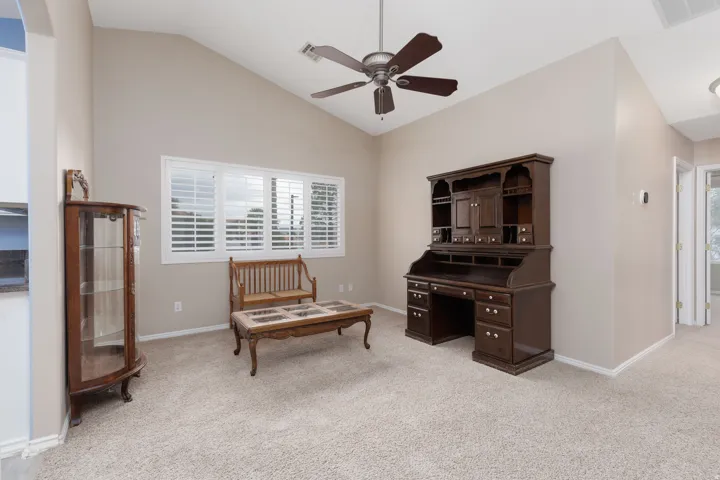 Vaulted ceiling with a ceiling fan, white window shutters, and neutral-toned carpeting