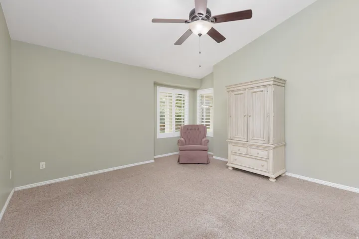 Vaulted ceiling with a ceiling fan, bay window with plantation shutters, and carpeted flooring