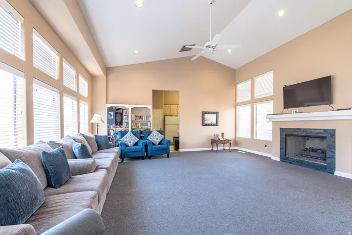Vaulted ceiling with a ceiling fan, fireplace with a stone surround and white mantel, recessed lighting, and expansive windows