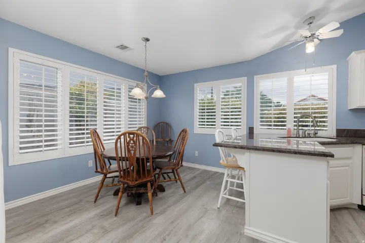 Window wall with white plantation shutters, wood-finish flooring, kitchen island with dark stone countertop, and ceiling fan