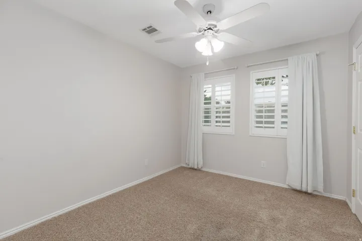 Light-colored carpeting, two windows with white plantation shutters, and a ceiling fan with integrated lighting