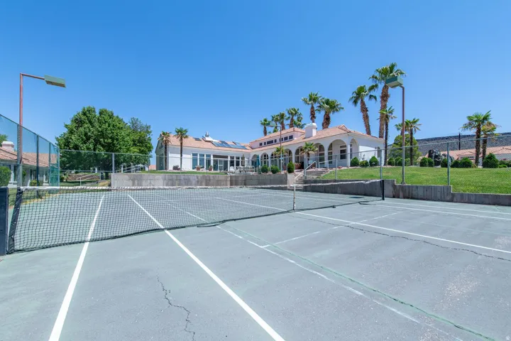 Outdoor tennis court with a net, bordered by fencing and concrete retaining walls