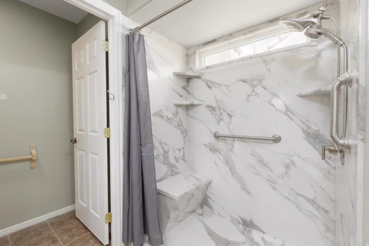 Shower with marble-finish walls, built-in bench, and integrated shelving