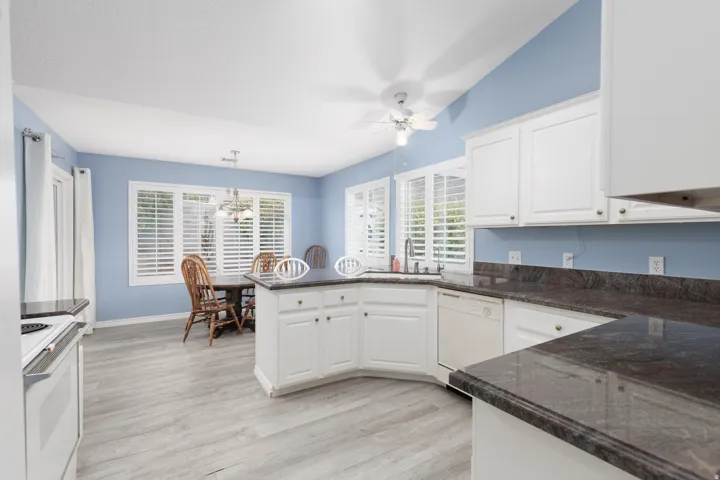 White cabinetry with dark countertops, wood-finish flooring, white appliances, and a ceiling fan