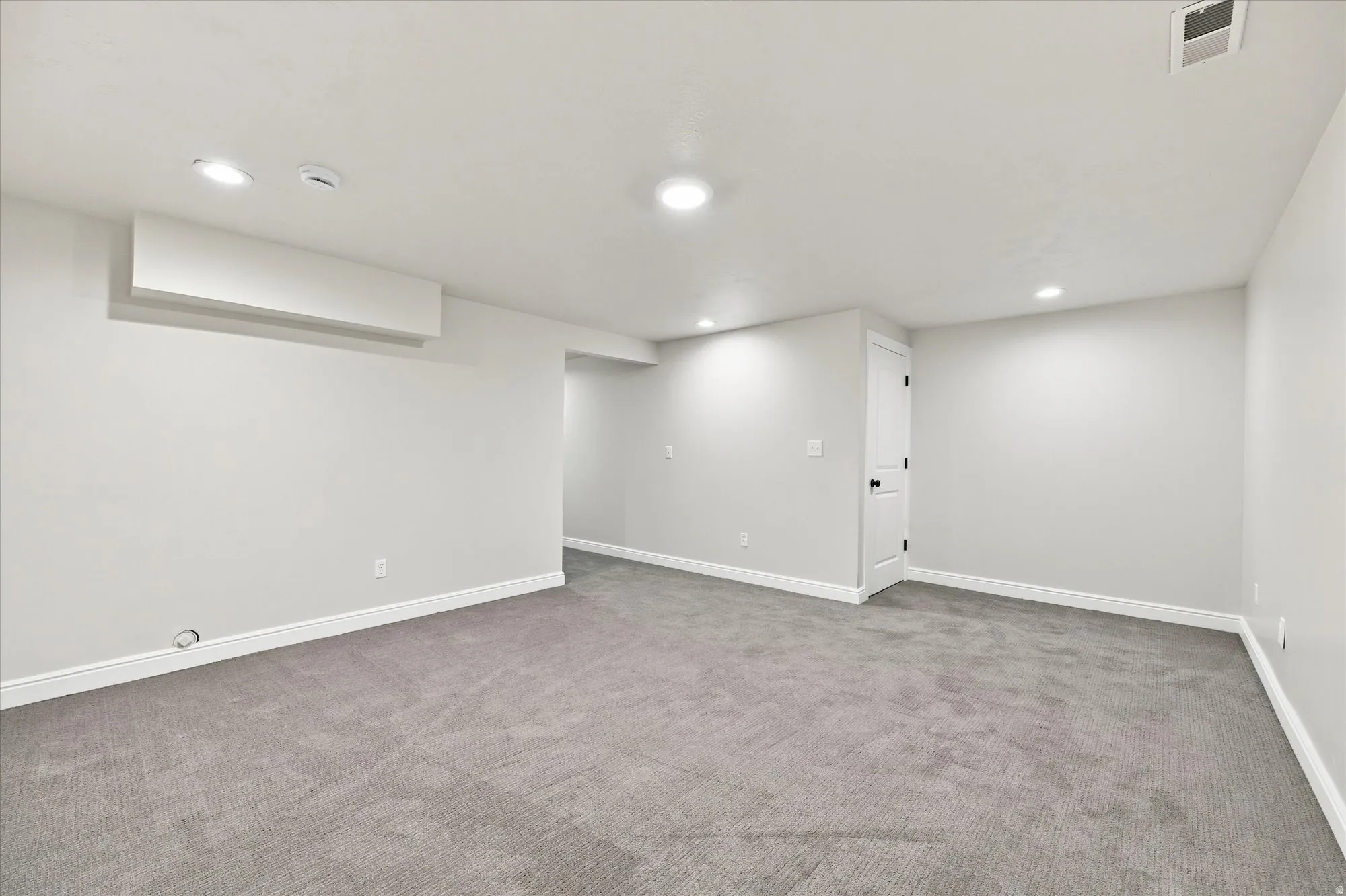 Recessed lighting, light gray wall finishes, gray carpeting, and a white interior door with black hardware