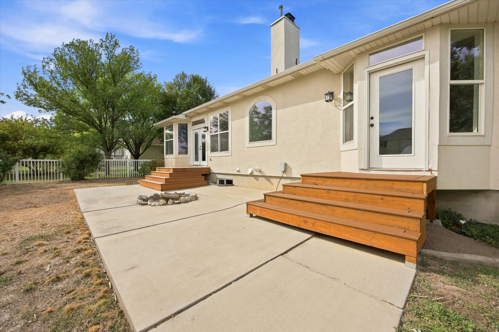 Spacious concrete patio with custom wood-finish built-in seating, fire pit area, and mature landscaping