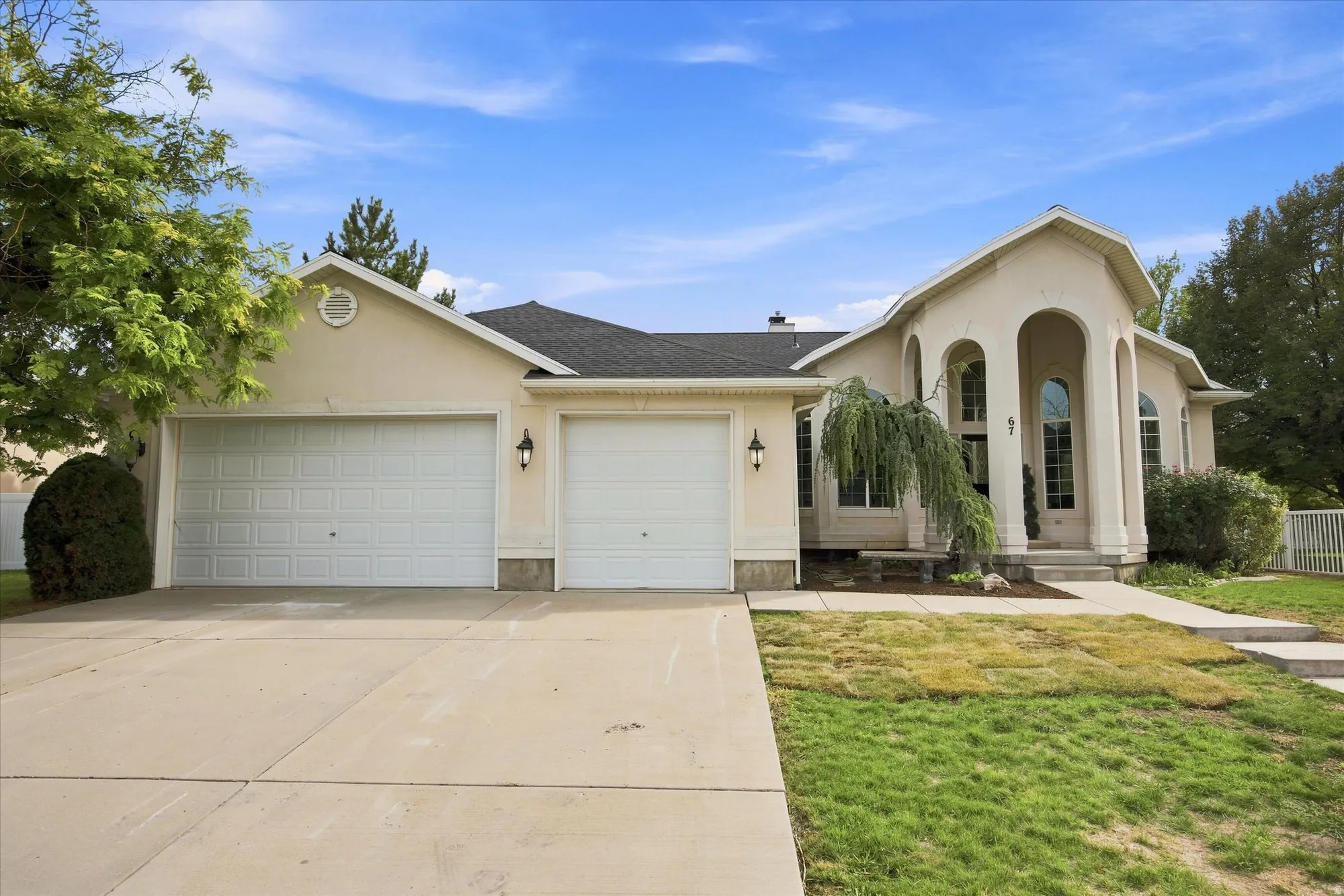 Stucco exterior featuring a two-car garage, concrete driveway, arched window details, and mature landscaping