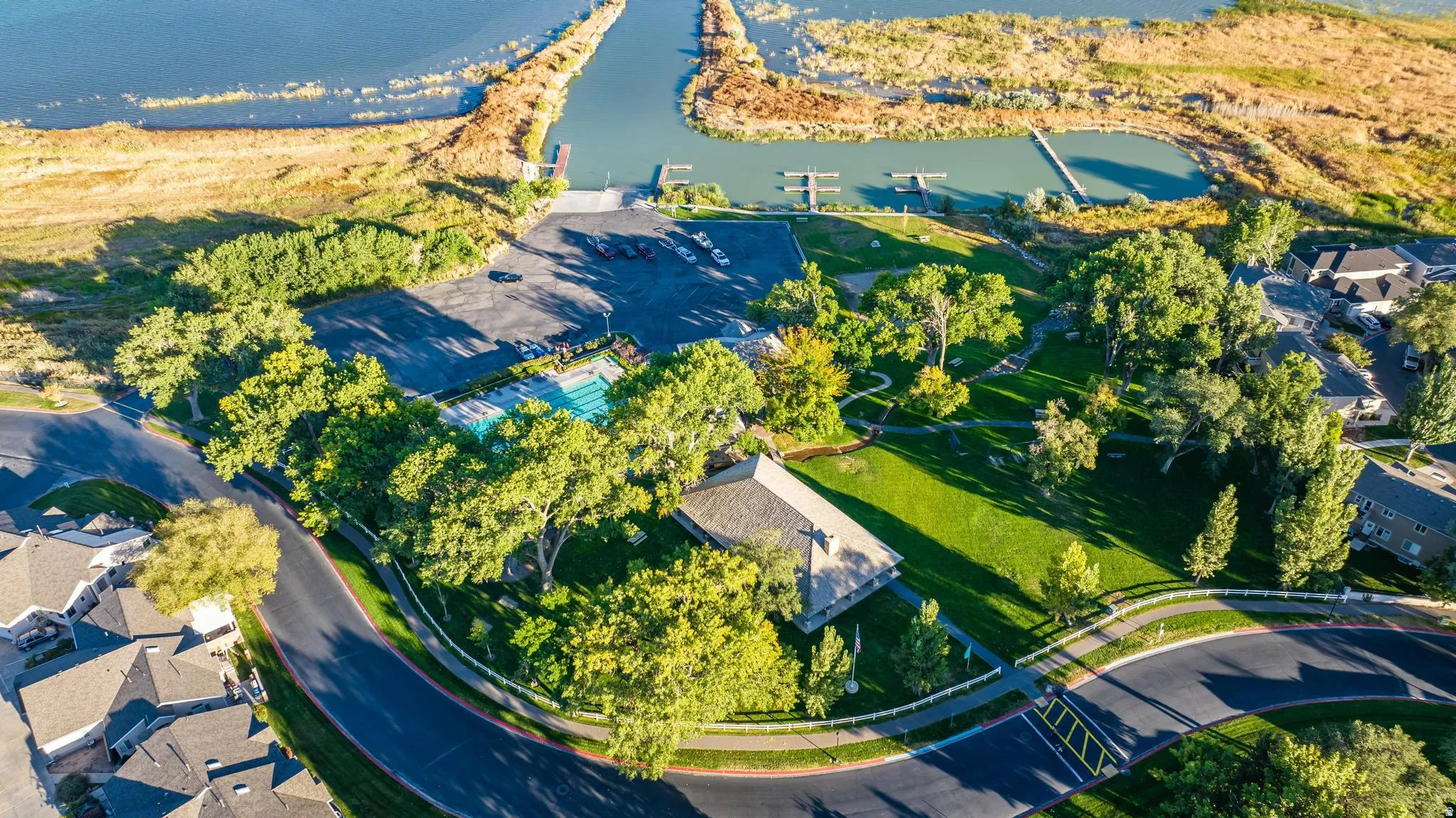 Outdoor swimming pool, marina with docks, expansive green spaces, shaded trees, and paved roads