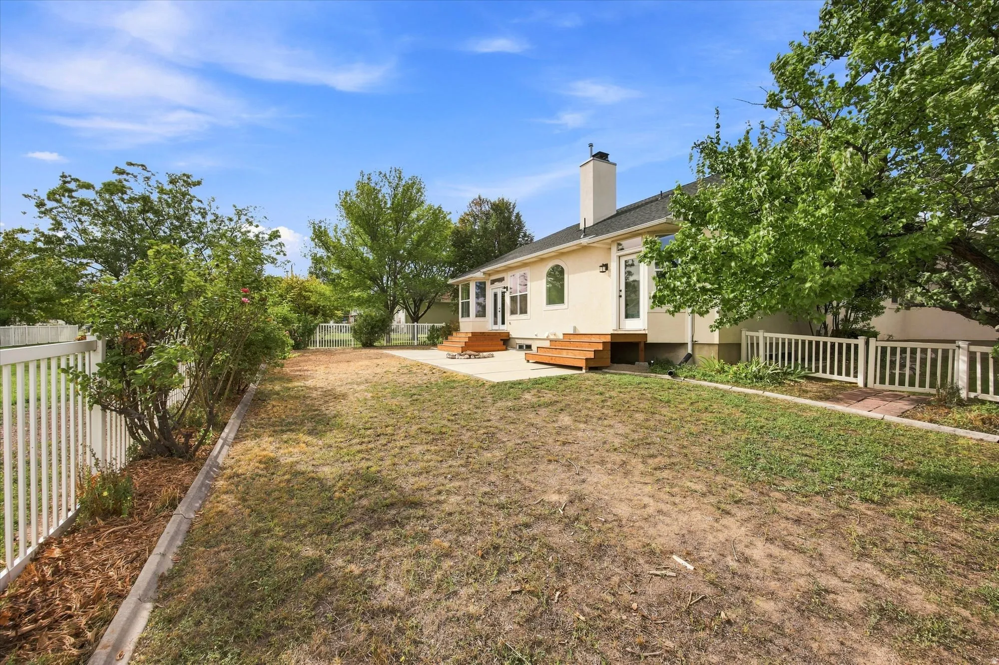 Expansive backyard with a manicured lawn, established trees, and white picket fencing