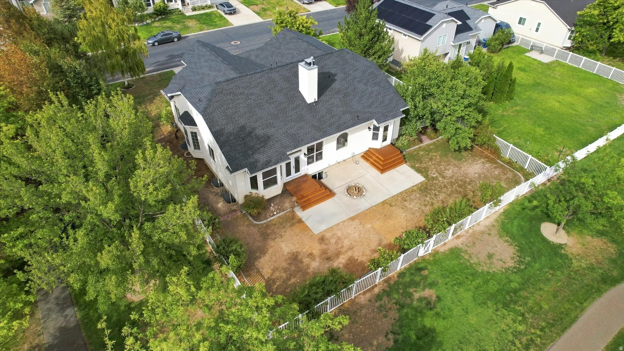 White exterior with a dark shingle roof, featuring two wood-finish decks, a concrete patio, and a fire pit area