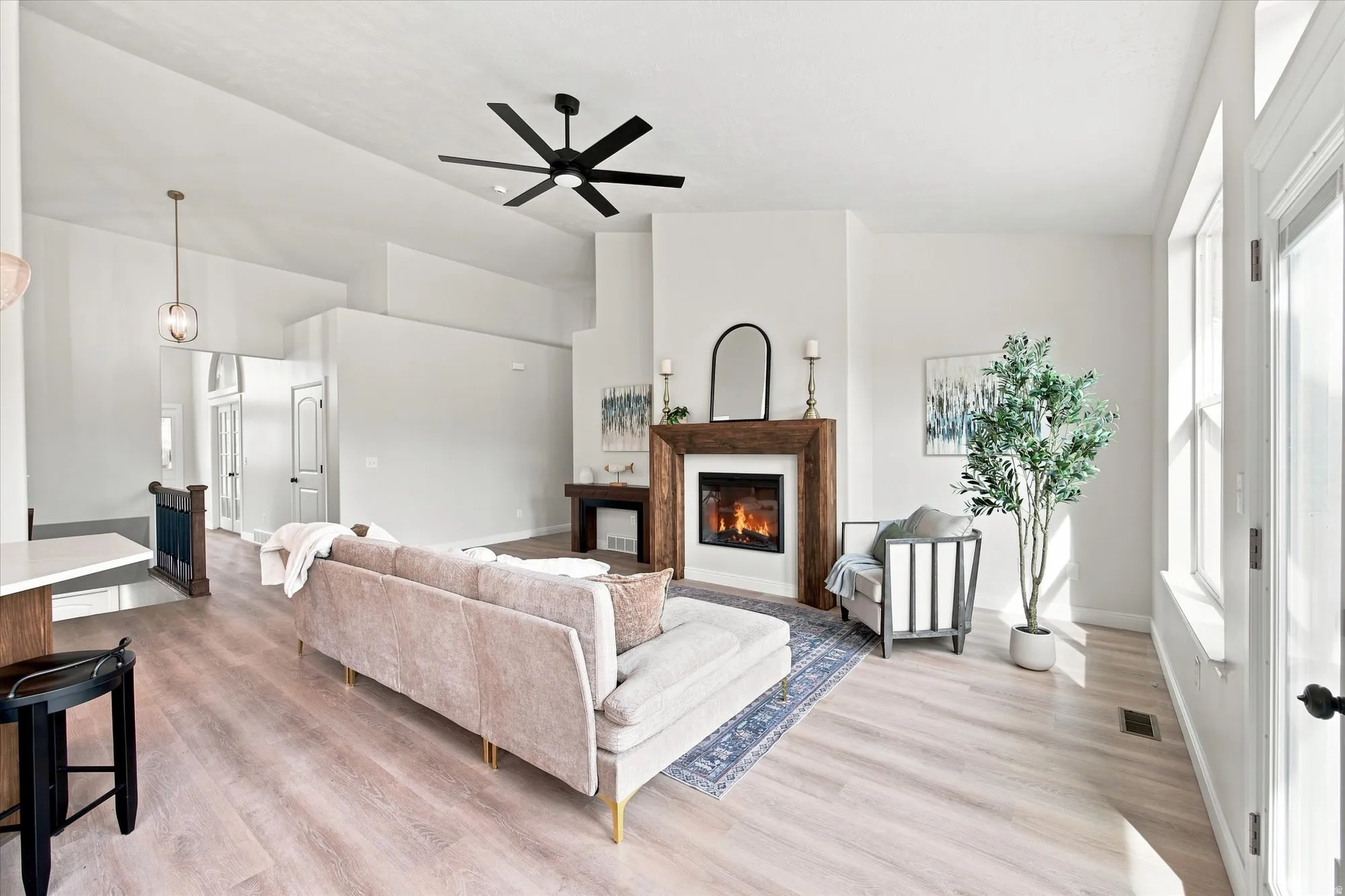 Vaulted ceiling with a black ceiling fan, wood-finish flooring, and a fireplace with a wood mantel