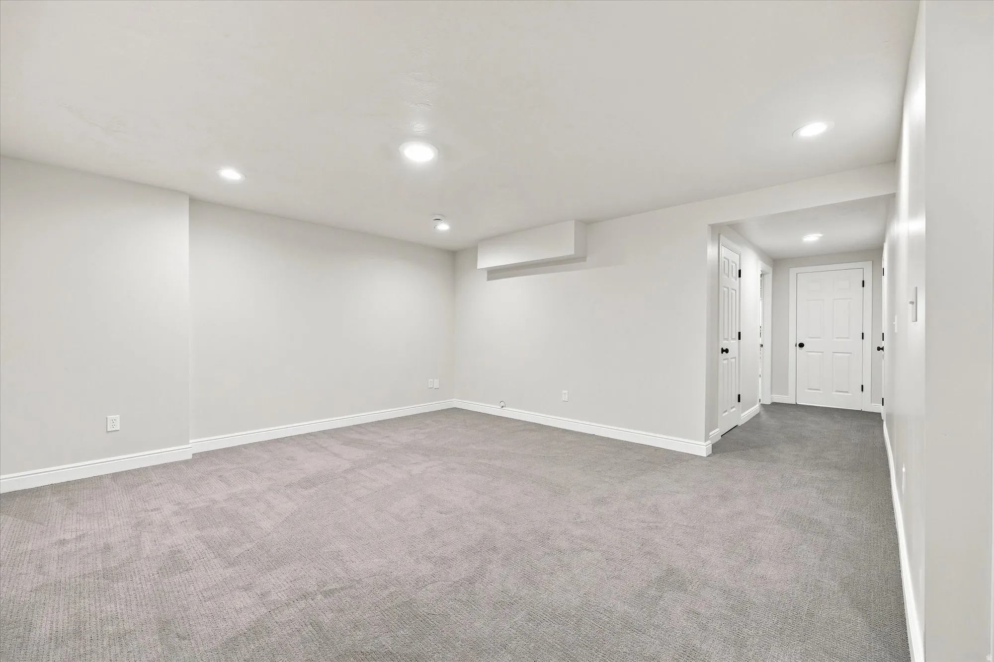 Recessed lighting illuminates the carpeted flooring and white walls, complemented by white doors with black hardware