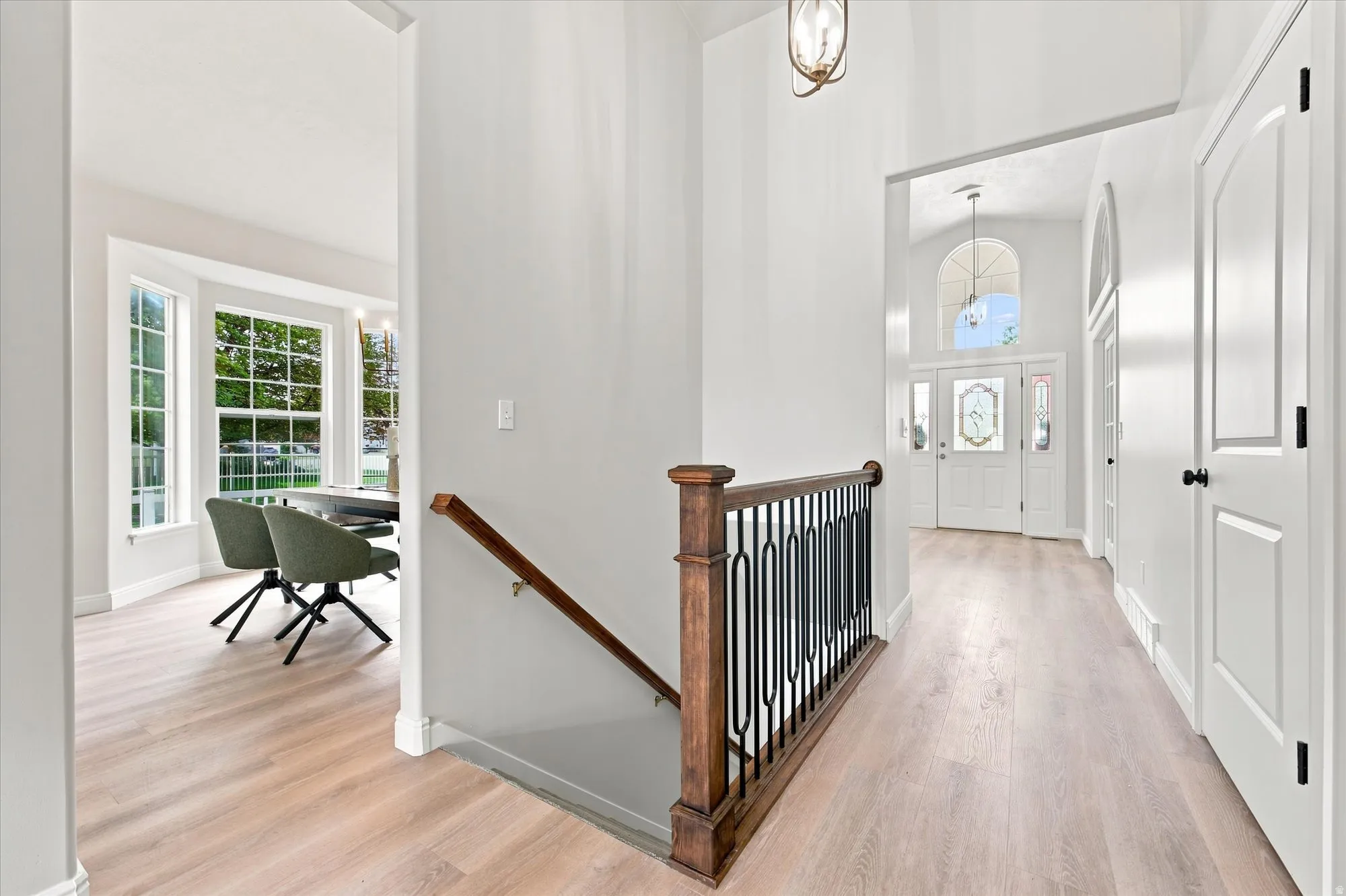Light wood-finish flooring throughout, bay windows with grid patterns, and a wooden staircase railing with black iron balusters