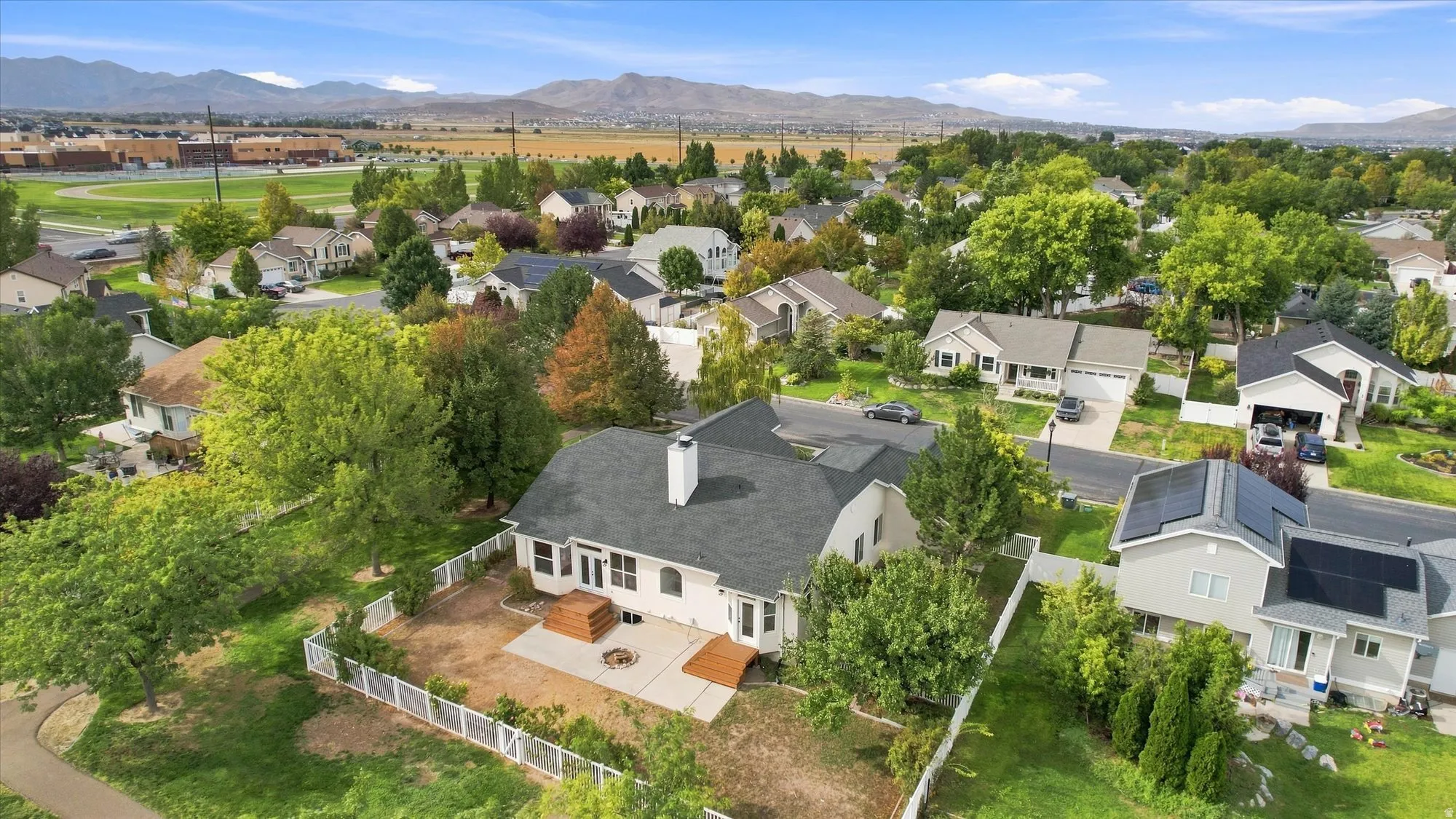 Expansive backyard featuring a white picket fence, concrete patio, and a wood deck