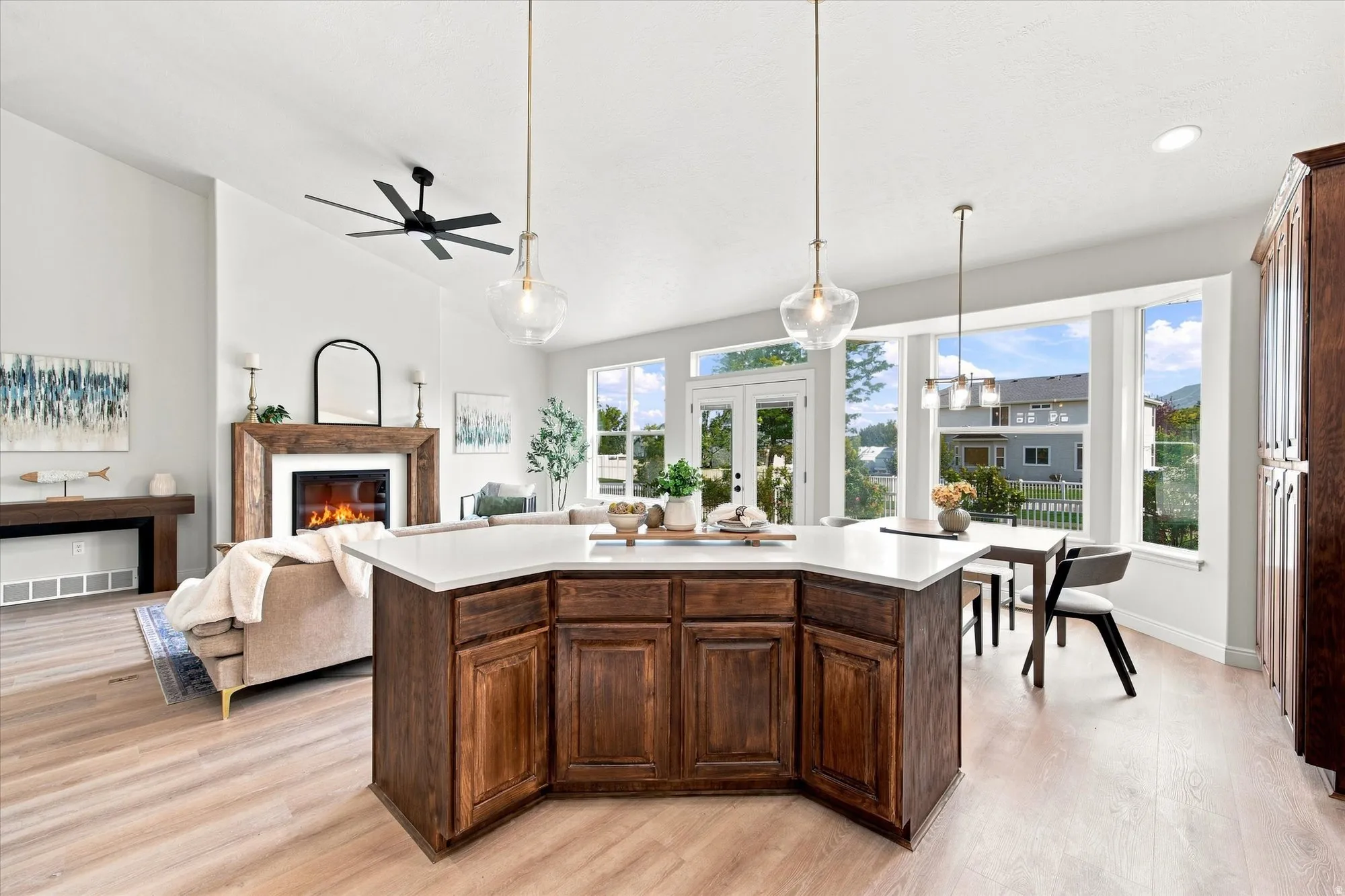 Open-concept living space featuring a central island with a solid surface countertop, wood-finish flooring, a fireplace with a wood mantel, and large windows