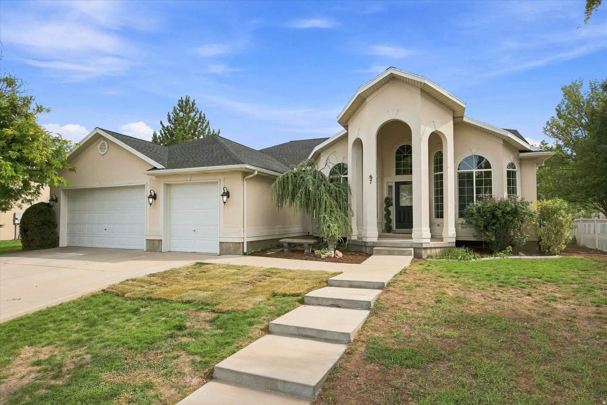 Stucco exterior with arched entryway, two attached garage bays, multiple arched windows, and a concrete pathway