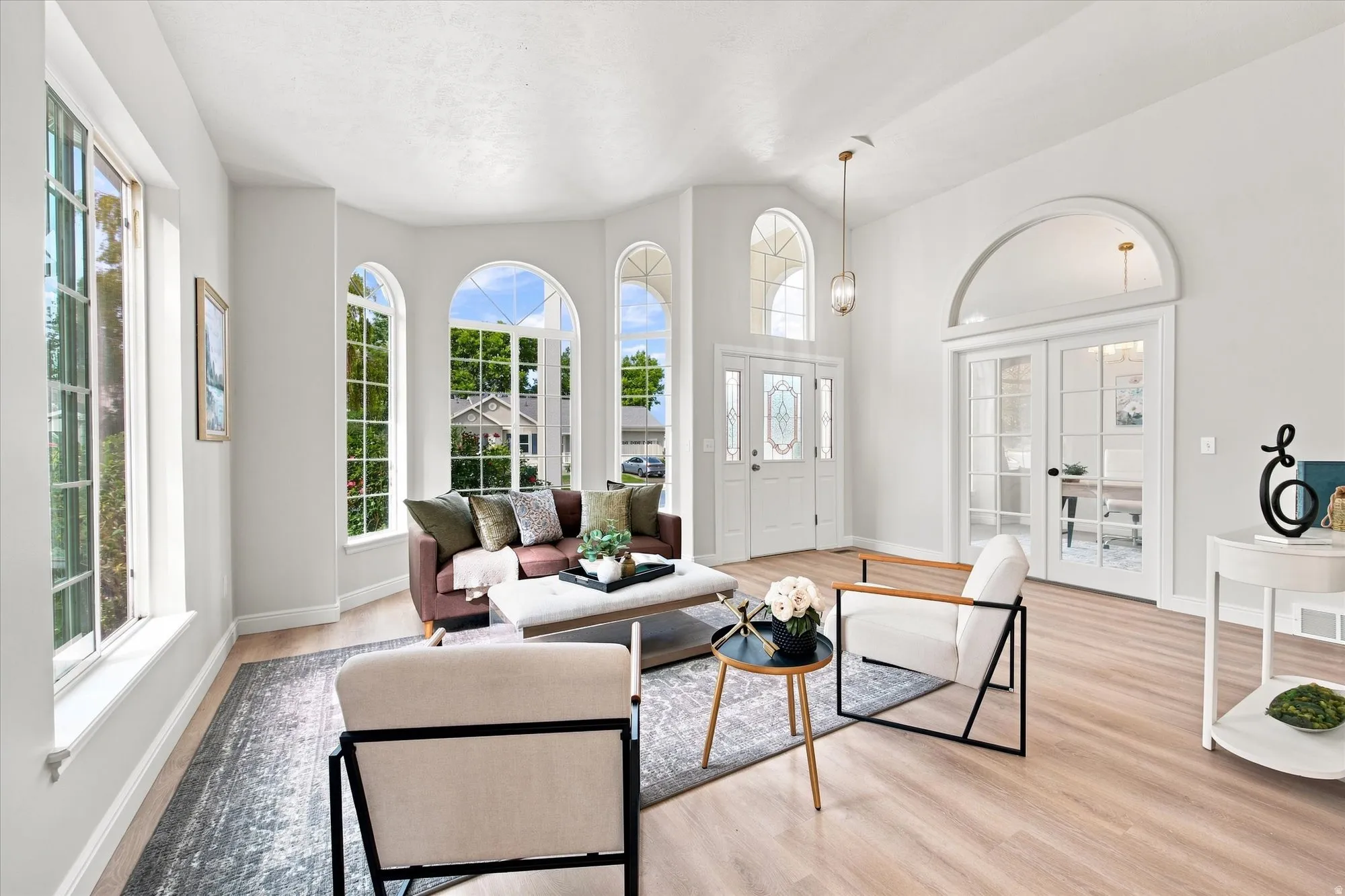 Vaulted ceilings, light wood-finish flooring, arched windows, and French doors with transoms