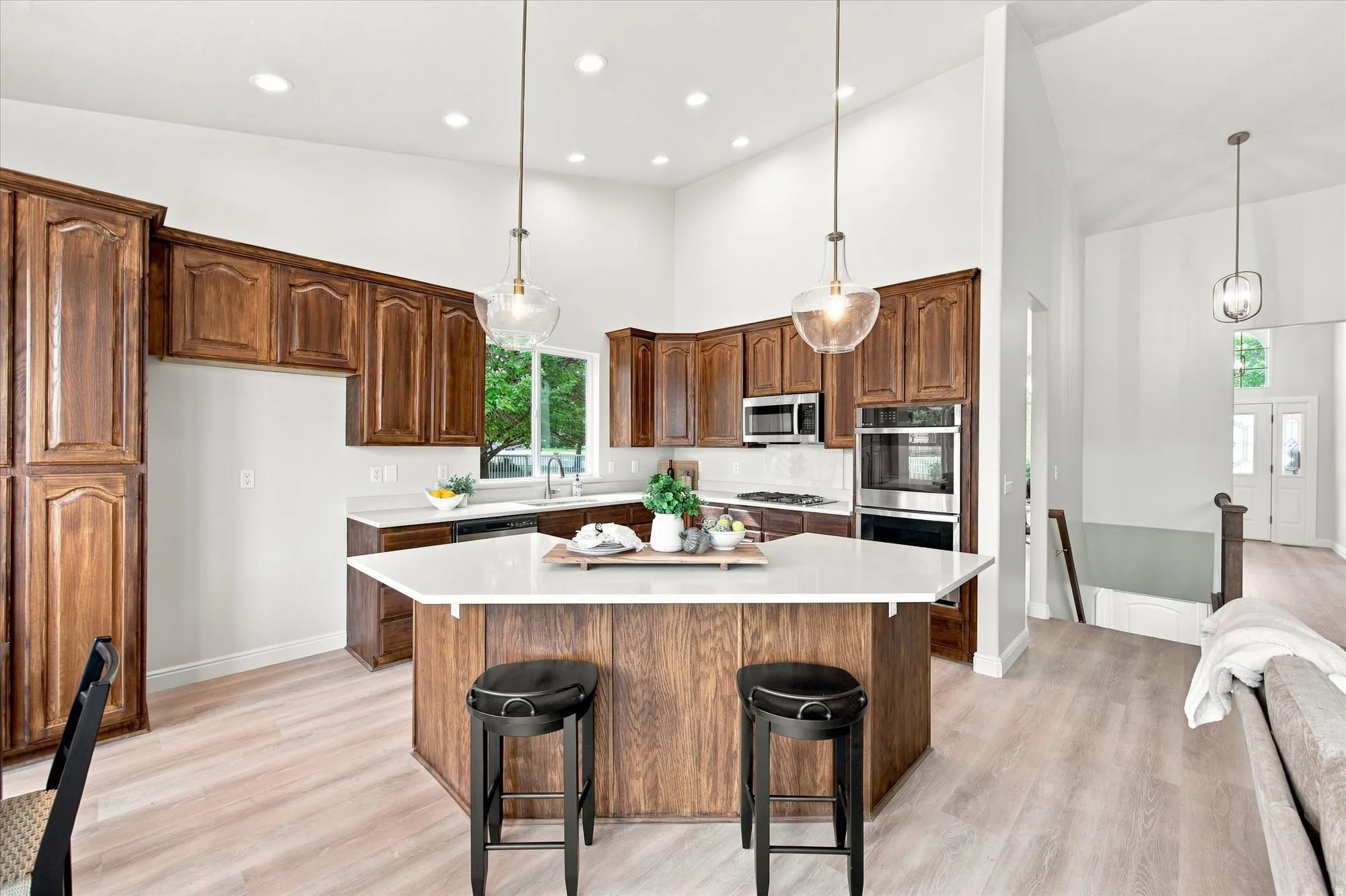 Spacious kitchen featuring wood cabinetry, white countertops, built-in stainless steel appliances, and a central island with pendant lighting