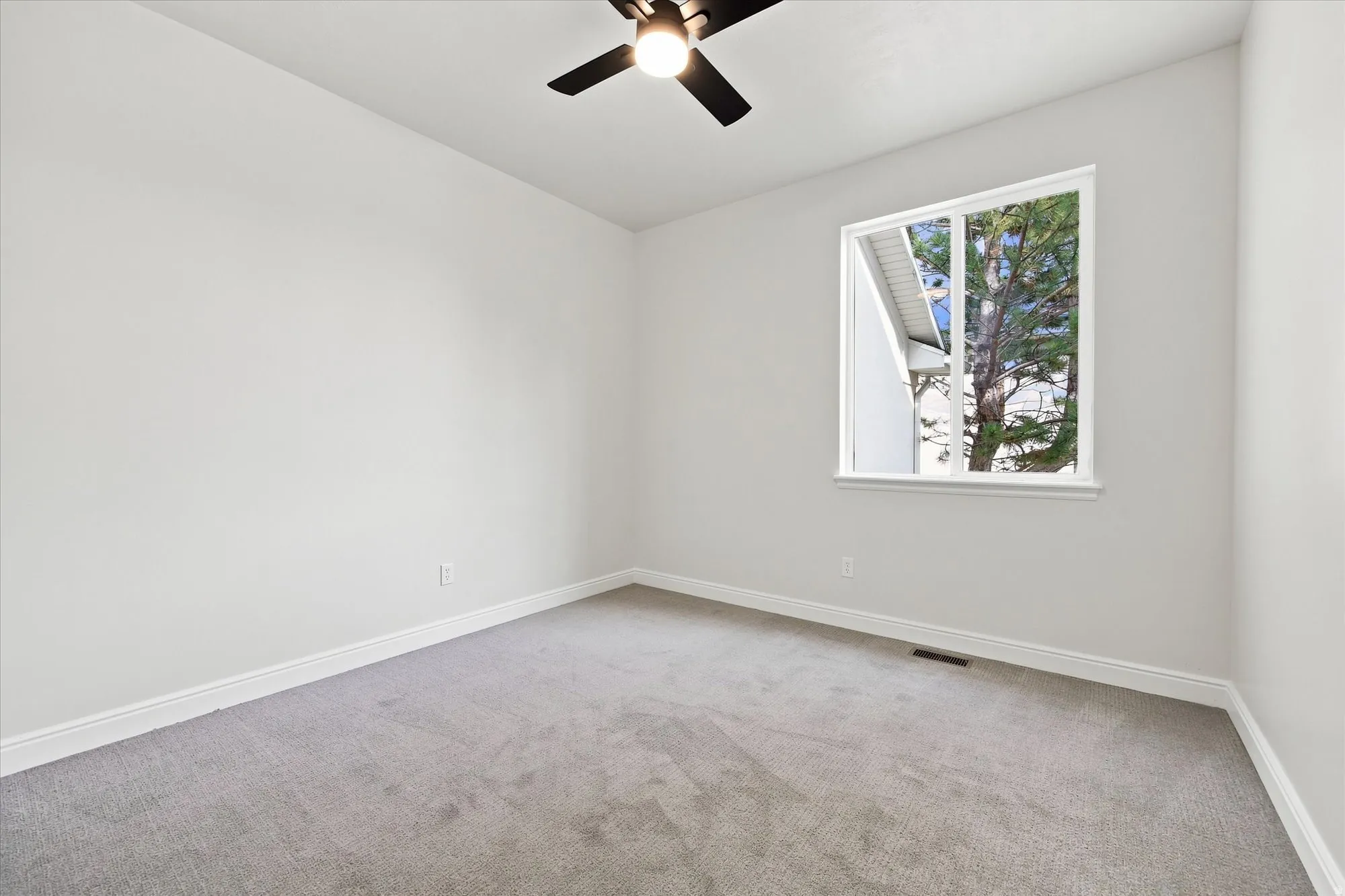Recessed window framing exterior greenery, ceiling fan with integrated lighting, gray carpet flooring, and white painted walls