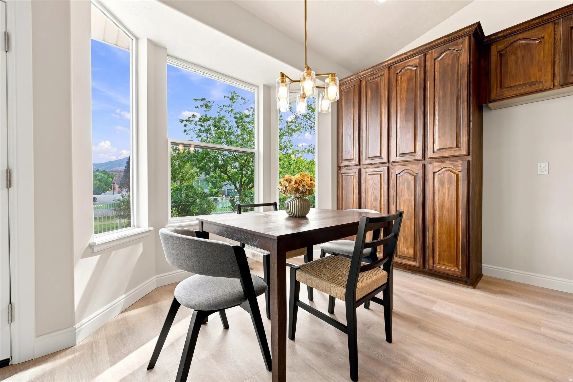 Bay window with white trim, built-in wooden cabinetry, light wood-finish flooring, and a contemporary ceiling light fixture