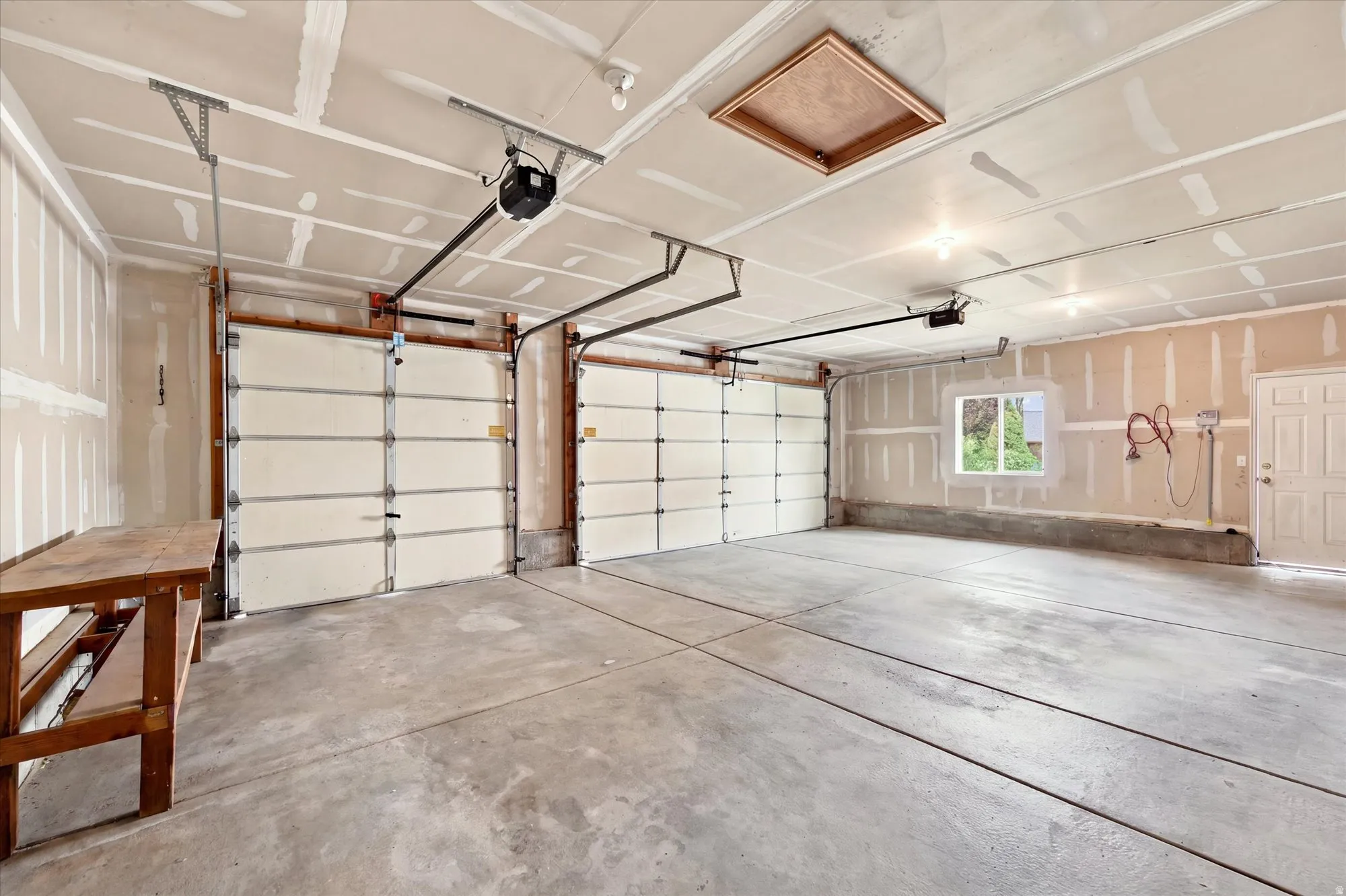 Two-car garage featuring concrete flooring, automatic garage door openers, a single window, and a built-in workbench