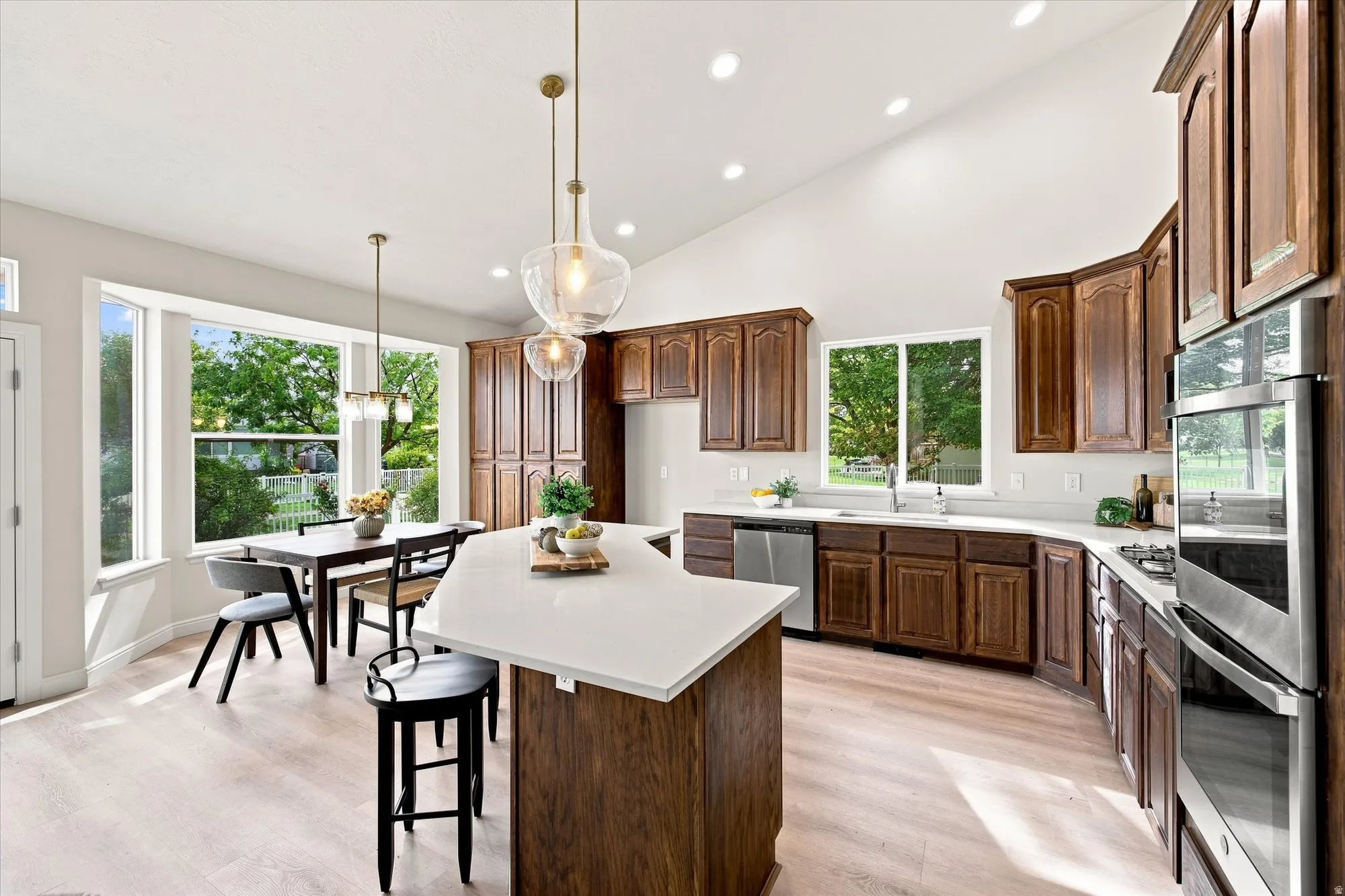 Spacious kitchen with a vaulted ceiling, wood-finish flooring, recessed lighting, and a kitchen island with a light-toned countertop