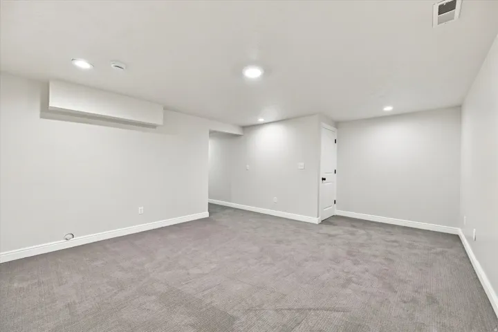 Recessed lighting, light gray wall finishes, gray carpeting, and a white interior door with black hardware