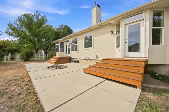 Spacious concrete patio with custom wood-finish built-in seating, fire pit area, and mature landscaping