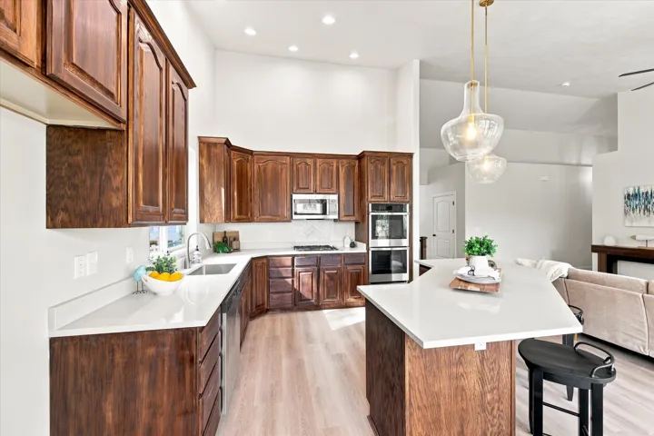 Kitchen featuring wood cabinetry, light-toned countertops, integrated stainless steel appliances, and wood-finish flooring