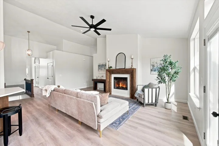 Vaulted ceiling with a black ceiling fan, wood-finish flooring, and a fireplace with a wood mantel