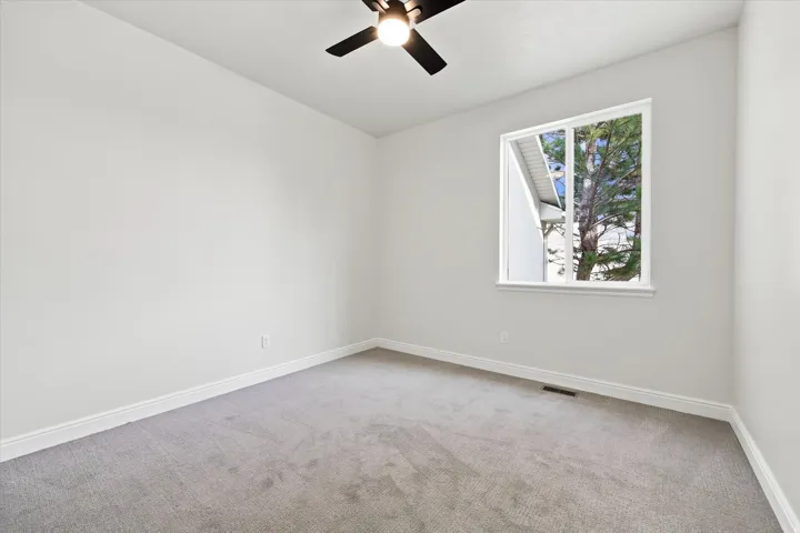 Recessed window framing exterior greenery, ceiling fan with integrated lighting, gray carpet flooring, and white painted walls