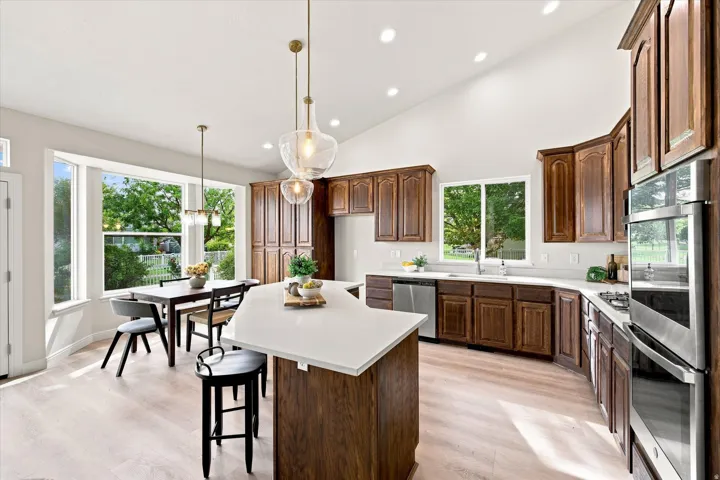 Spacious kitchen with a vaulted ceiling, wood-finish flooring, recessed lighting, and a kitchen island with a light-toned countertop