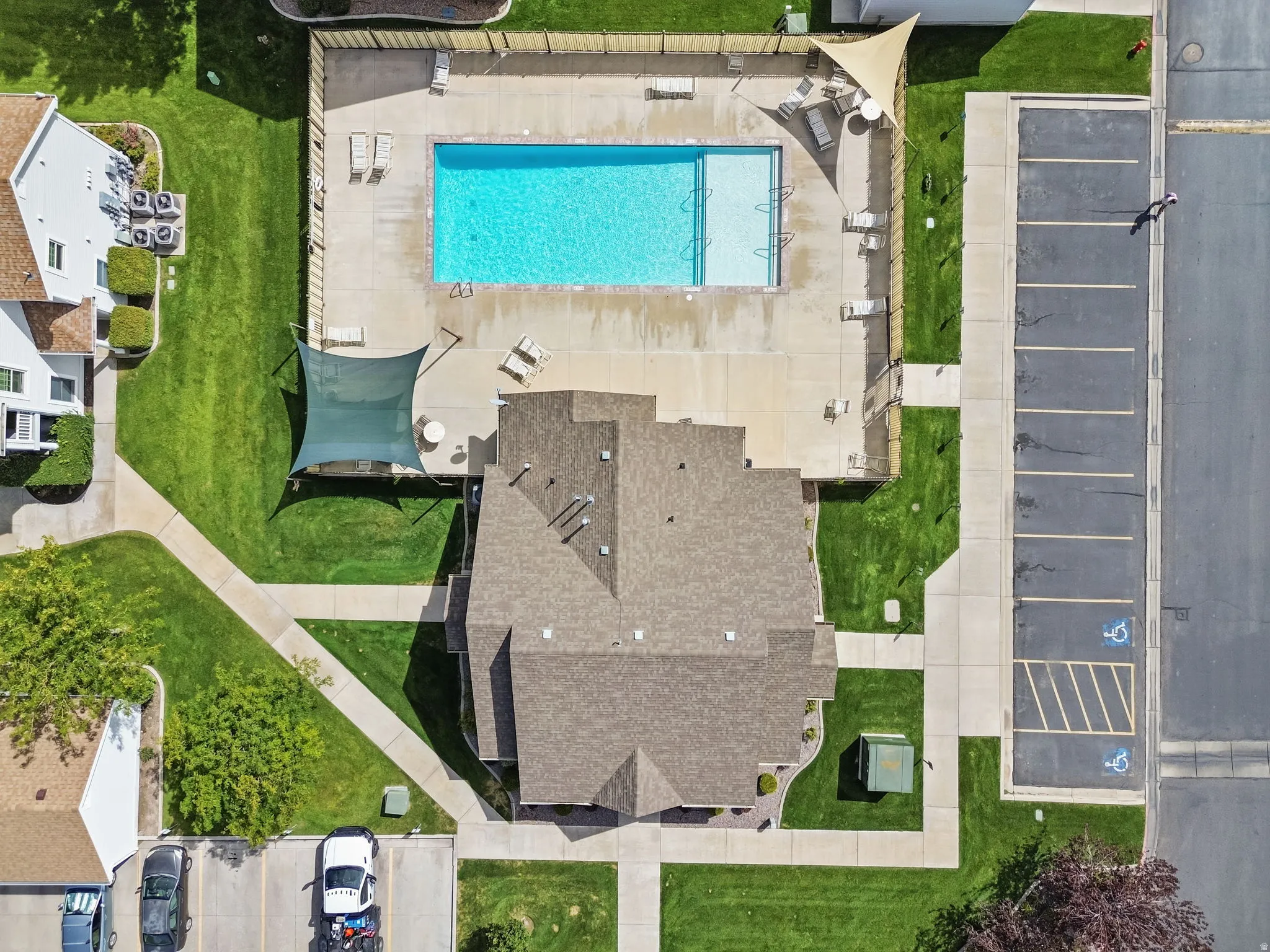 Community swimming pool with surrounding concrete patio, fenced perimeter, and adjacent shaded seating areas