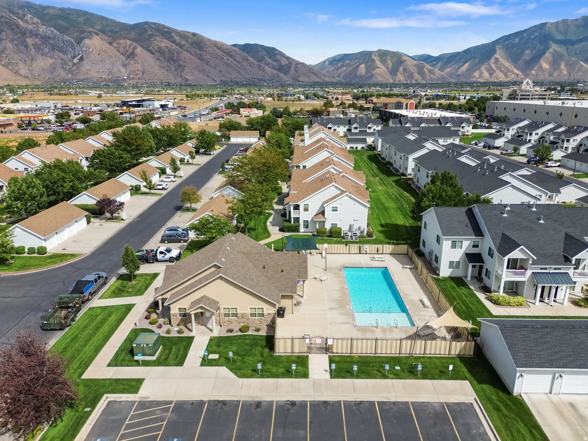 Community pool area with surrounding fencing, adjacent multi-story residences, and distant mountainous terrain