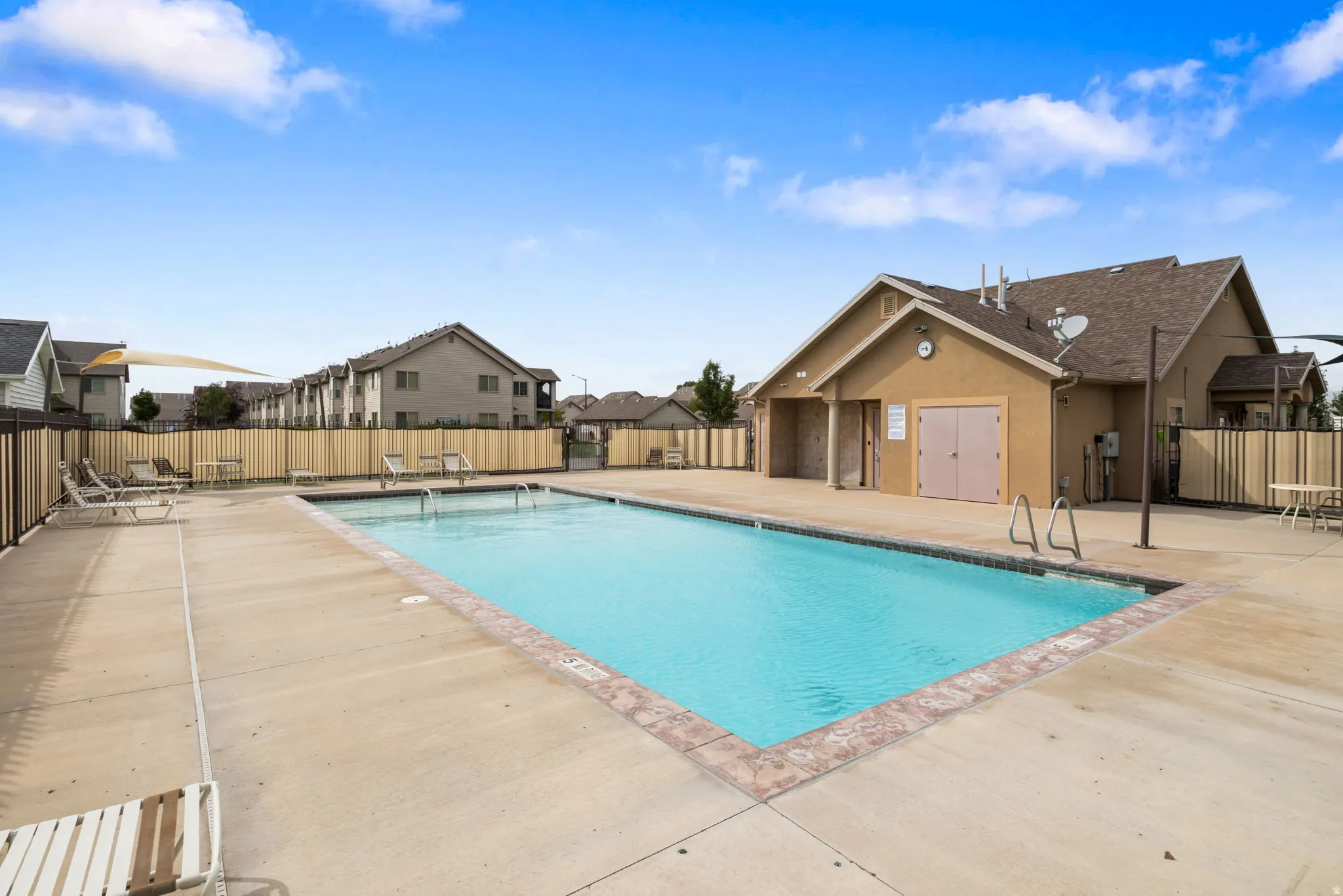 Expansive outdoor swimming pool with concrete decking, a tiled pool edge, and a stucco-finished pool house