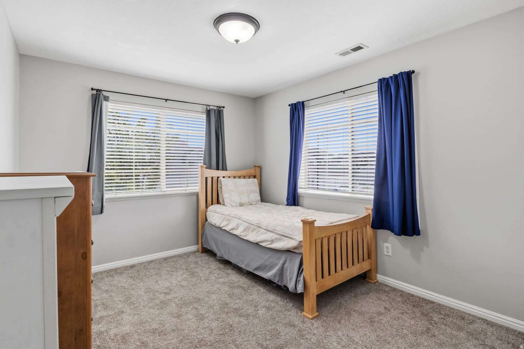 Two windows with blinds, gray wall paint, and gray carpet flooring