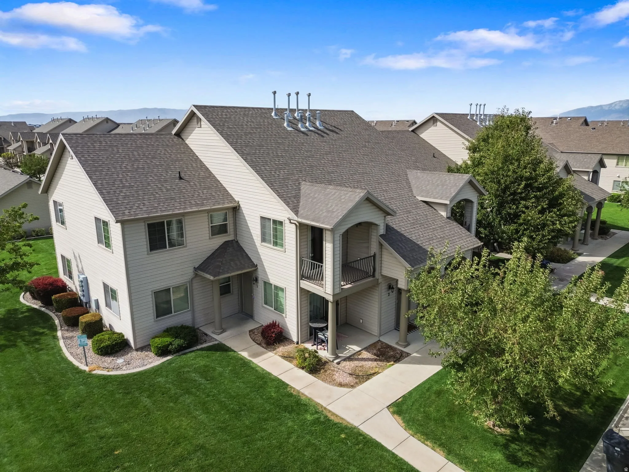 Multi-level residential building featuring light-toned siding, dark shingle roofing, and multiple balconies