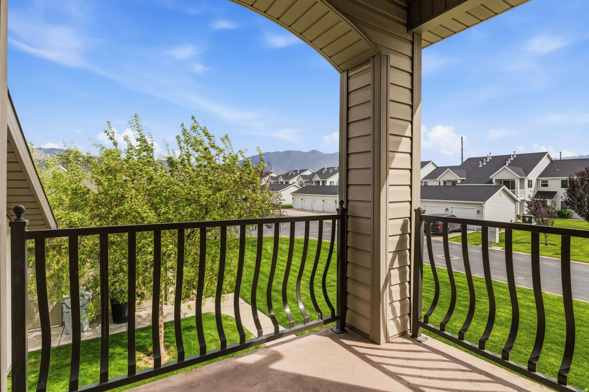 Balcony with black wrought iron railing, concrete flooring, and beige siding