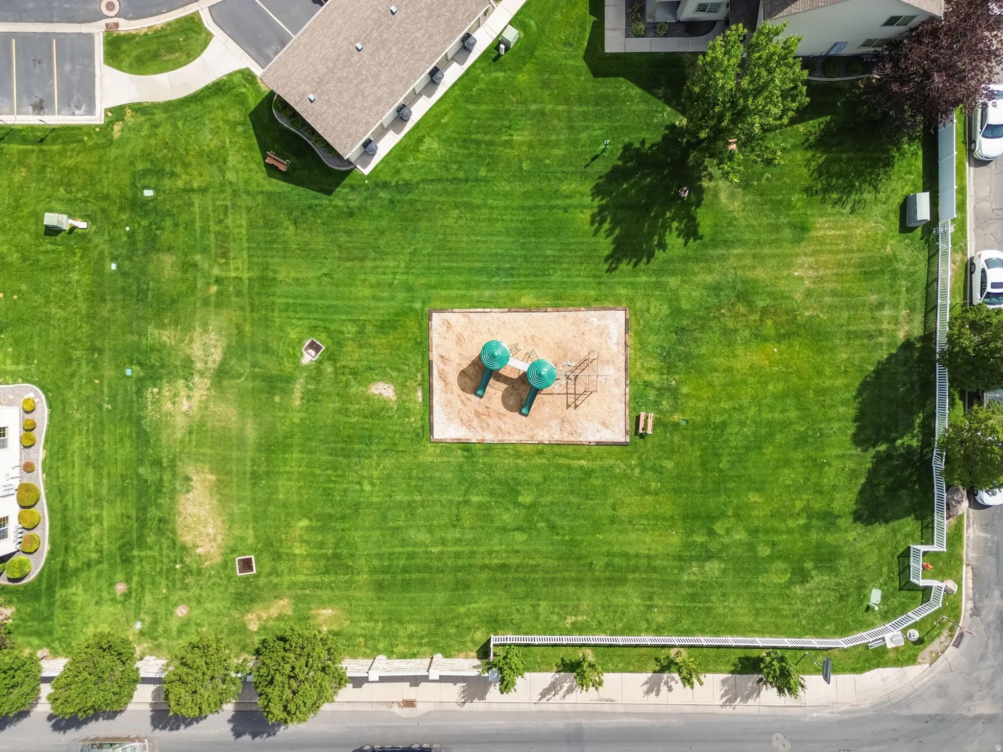 Expansive backyard featuring a manicured lawn with mature shade trees, a central sand-based play area with modern recreational equipment, and mature landscaping along the perimeter