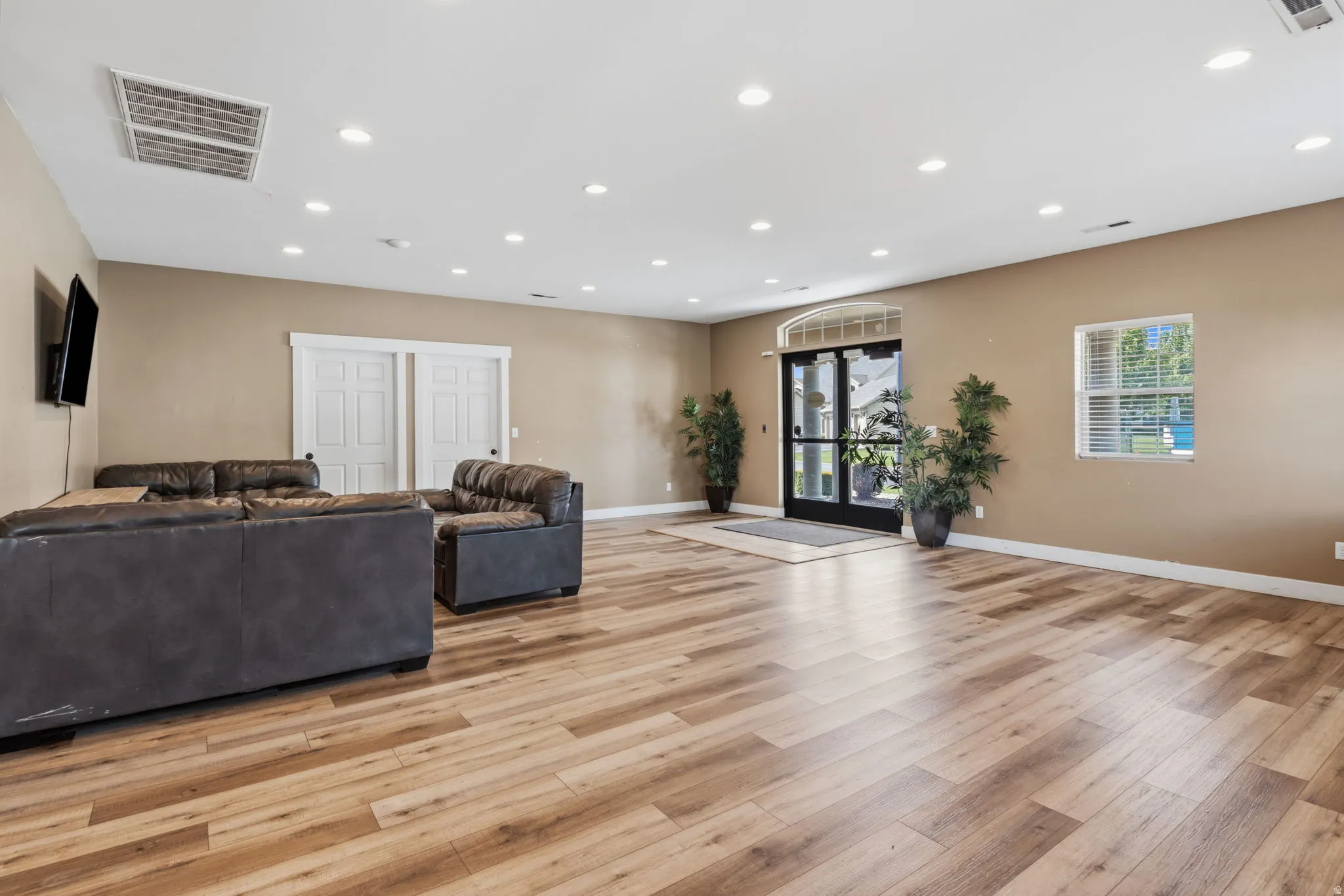 Spacious room featuring wood-finish flooring, recessed lighting, and a large arched entryway with double glass doors