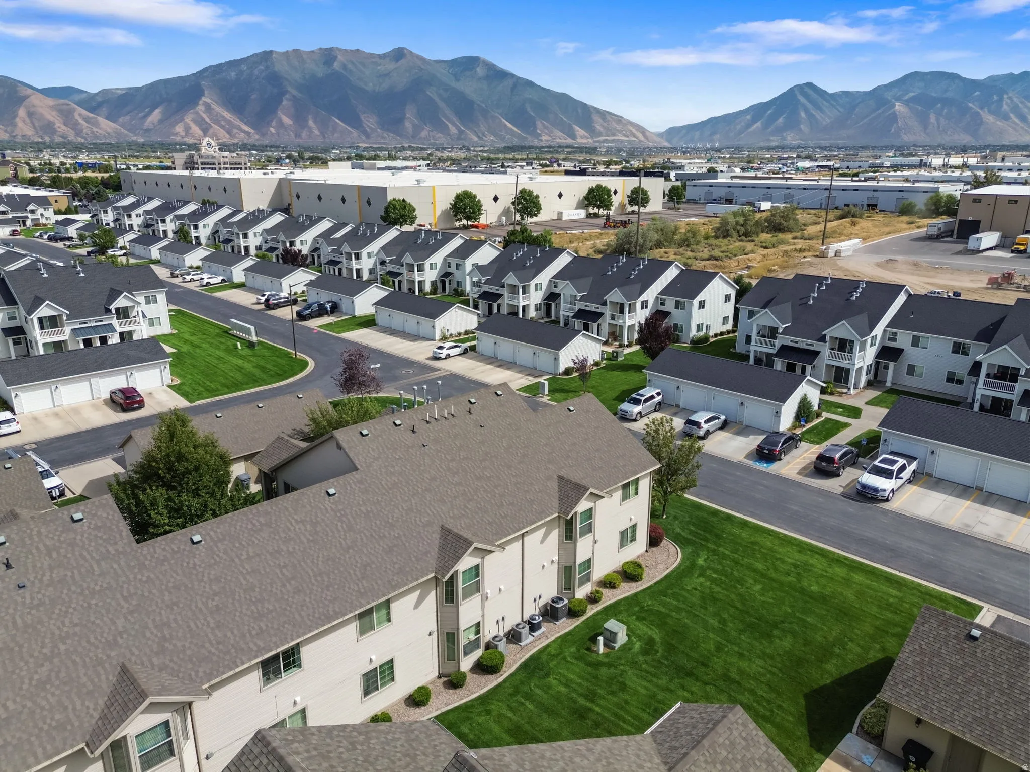 Expansive community featuring multiple residential buildings, detached garages, manicured green spaces, and paved roadways, all set against a distant mountain backdrop