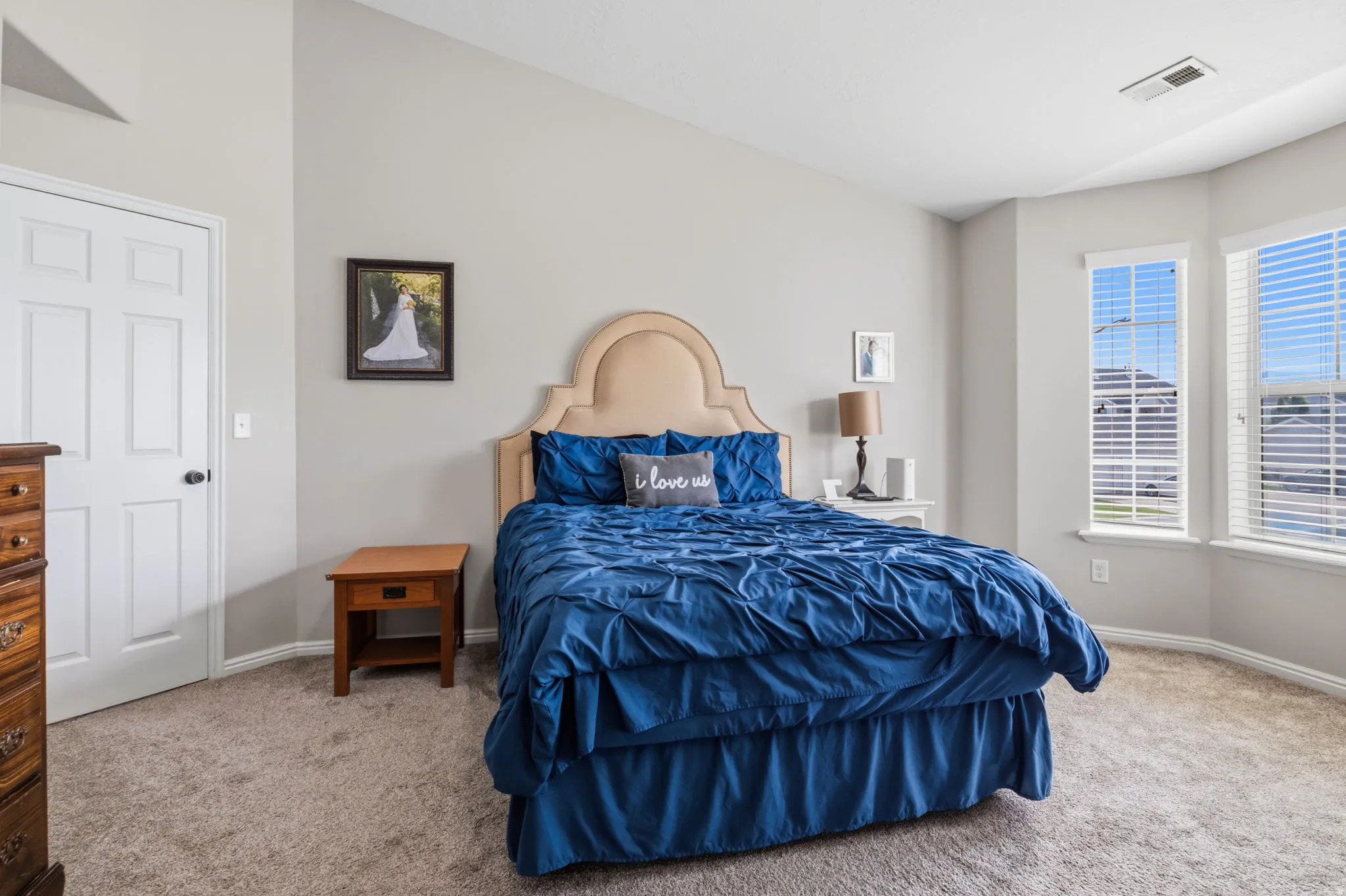 Vaulted ceilings, bay windows with blinds, light gray wall paint, and beige carpeting