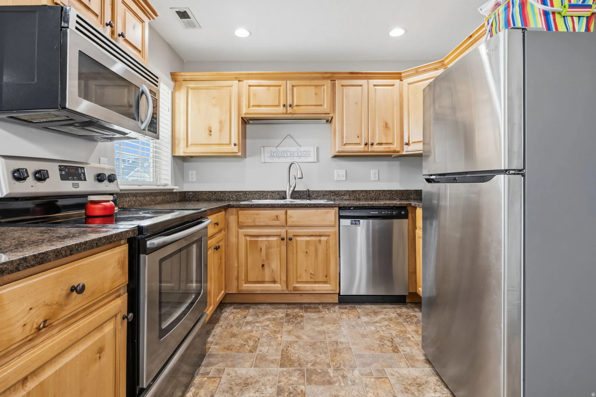 Full kitchen featuring wood cabinetry, stainless steel appliances, dark countertops, and a stainless steel sink with a gooseneck faucet