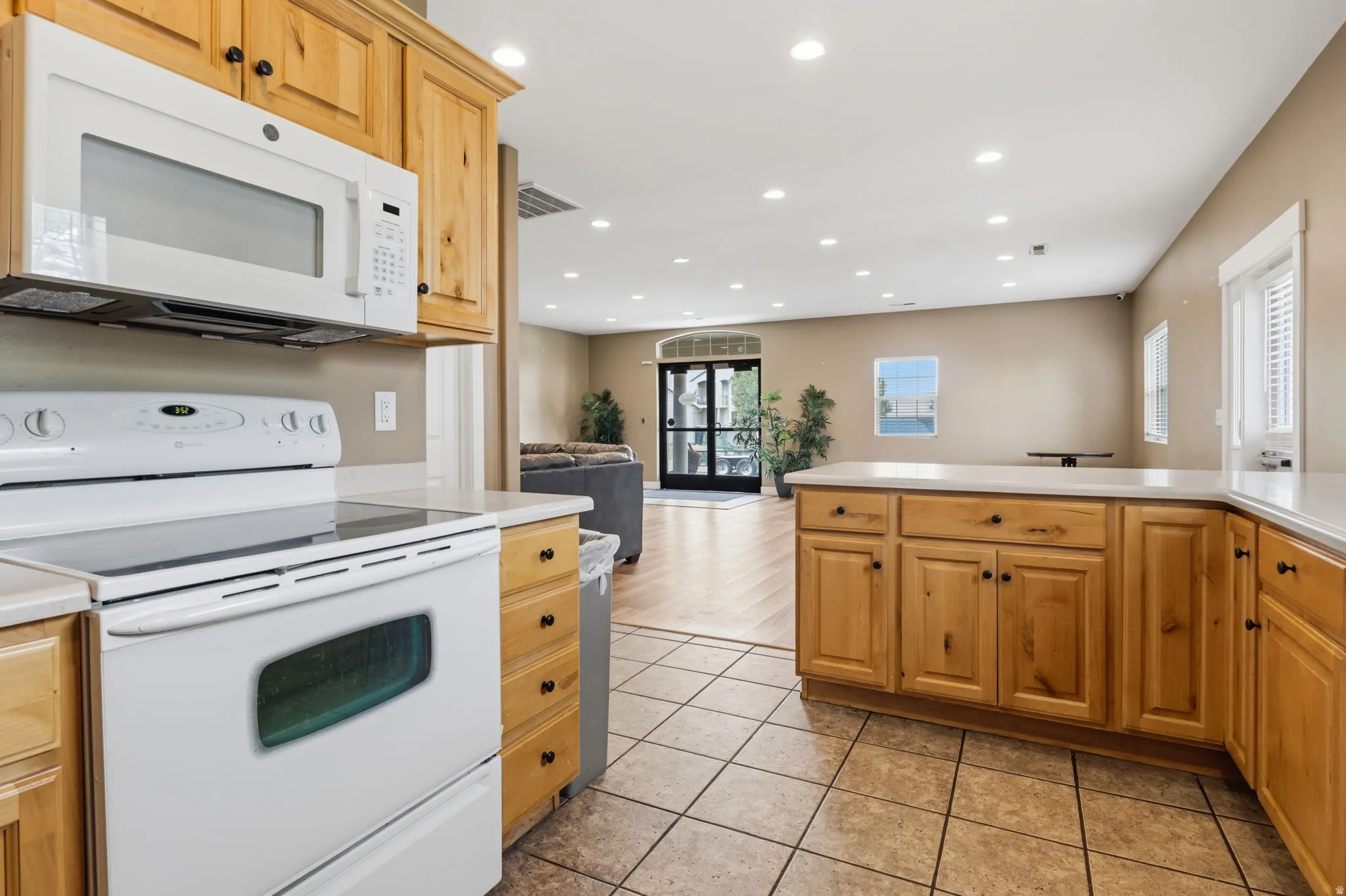 Kitchen featuring wood cabinetry, white appliances, light countertops, and tile flooring