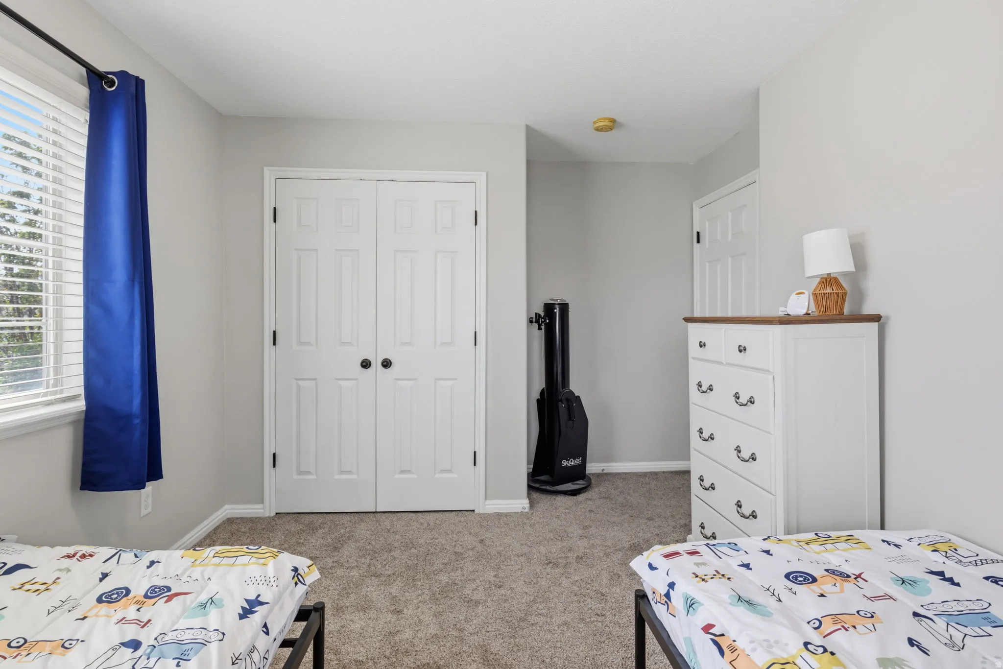Neutral wall color, carpeted flooring, white bi-fold closet doors with black hardware, white interior door, and a single window with blinds