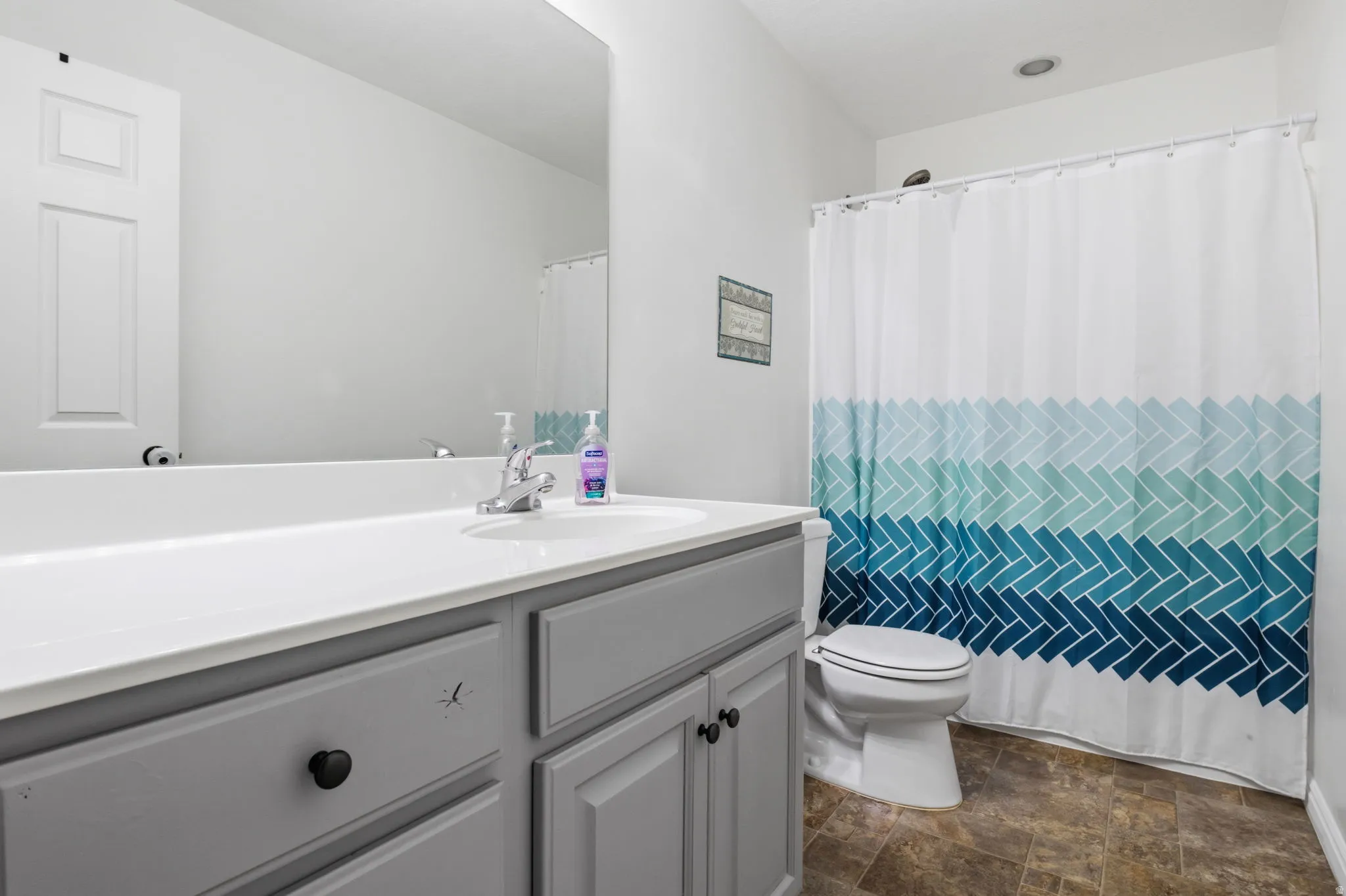 Bathroom featuring a single vanity with a white countertop, gray cabinetry, a wall-mounted mirror, and a commode