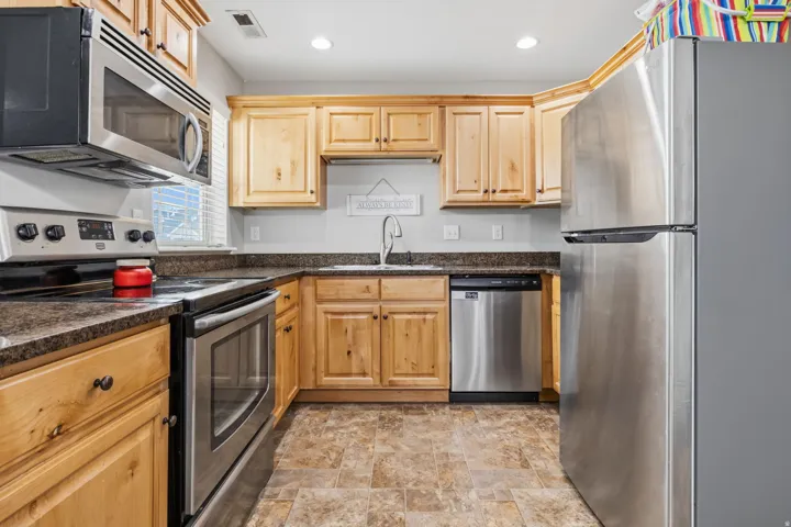 Full kitchen featuring wood cabinetry, stainless steel appliances, dark countertops, and a stainless steel sink with a gooseneck faucet