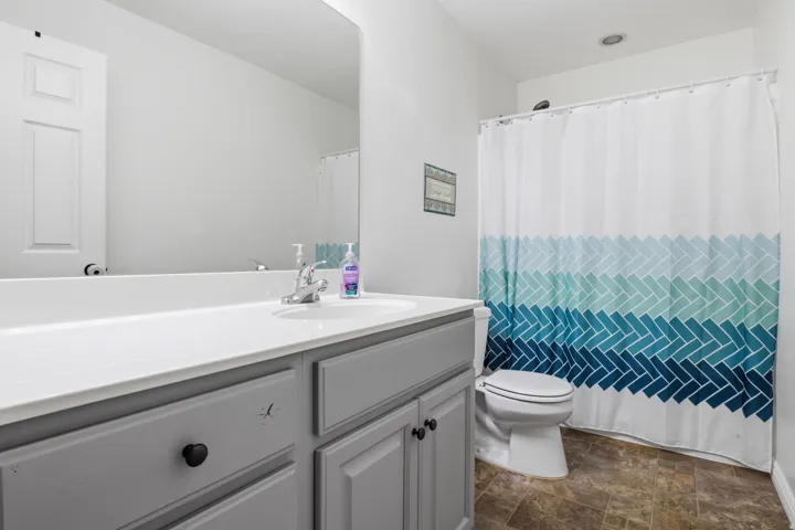 Bathroom featuring a single vanity with a white countertop, gray cabinetry, a wall-mounted mirror, and a commode