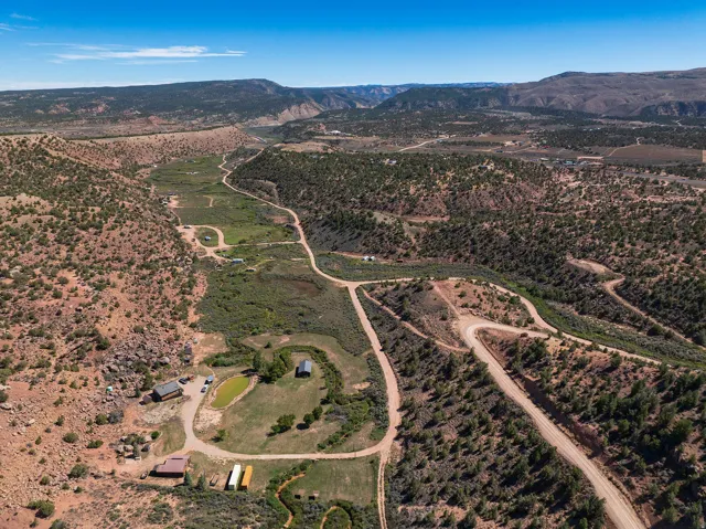 Expansive rural landscape featuring multiple structures, a pond, and unpaved roads