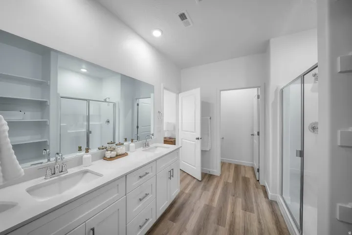 Double vanity with undermount sinks, wood-finish flooring, glass-enclosed shower, built-in shelving, and recessed lighting